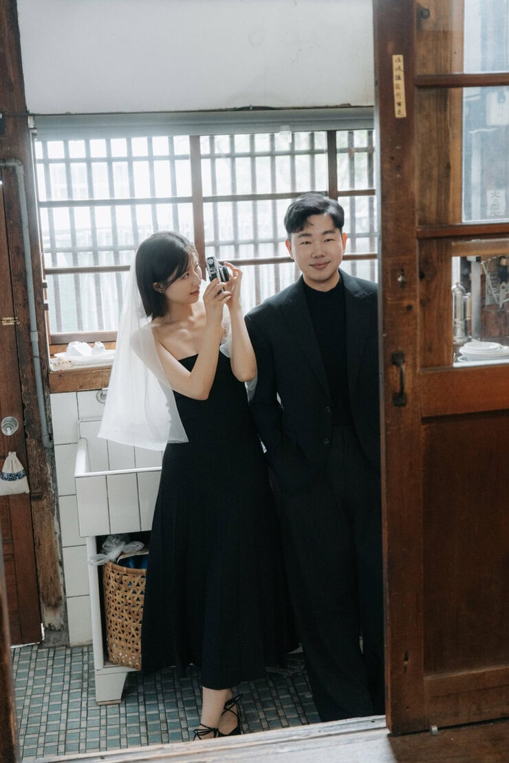 日系老宅婚紗攝影：身穿黑色禮服的新娘在老宅室內與花束互動的韓系棚拍婚紗照。